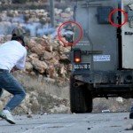 Mustafa Tamimi (left) a moment before his injury. Circled in red are the barrel of the gun and the projectile that hit him