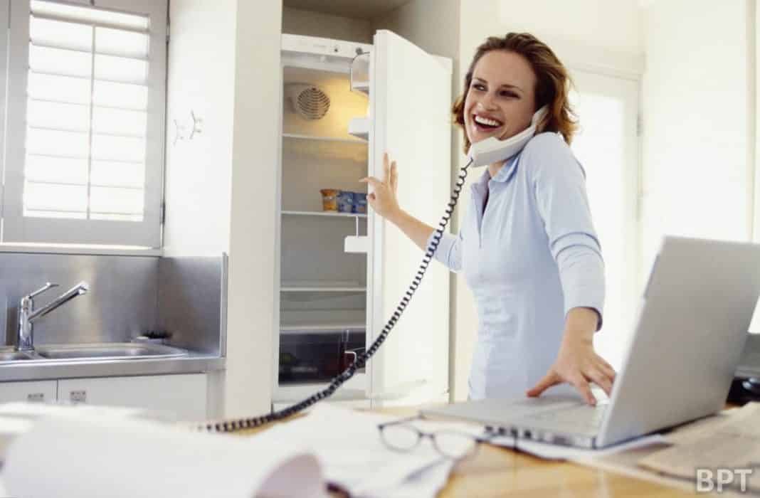Woman talking on telephone and working on laptop at home