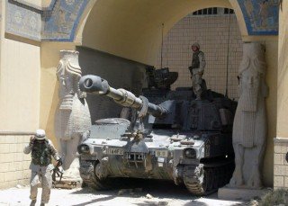 A US soldier stands on a Bradley tank stationed at the main entrance of the Iraqi National Museum as another soldier walks by in Baghdad 21 June 2003