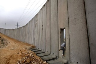 Palestinian boy climbs through an opening in Israel's wall near Jerusalem